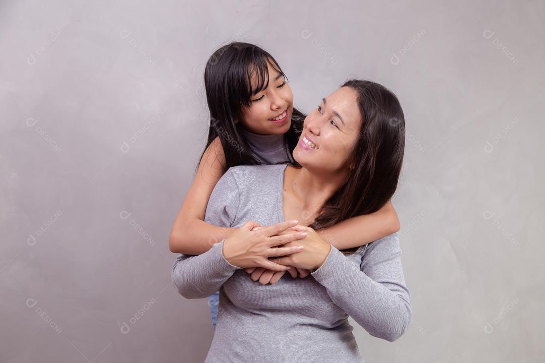 Mãe e filha abraçadas com camisetas cinzas em fundo bege