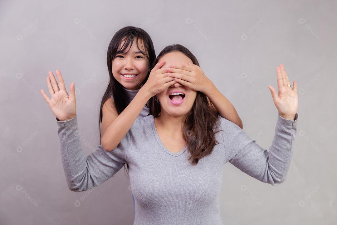 Mãe e filha abraçadas com camisetas cinzas em fundo bege