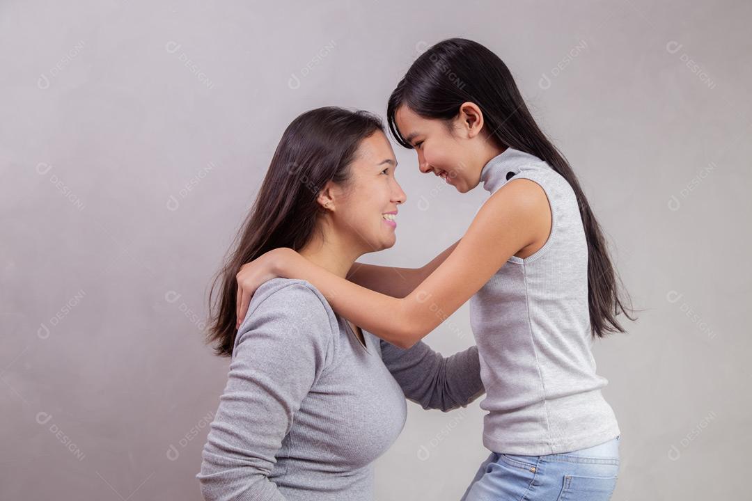 Mãe e filha abraçadas com camisetas cinzas em fundo bege