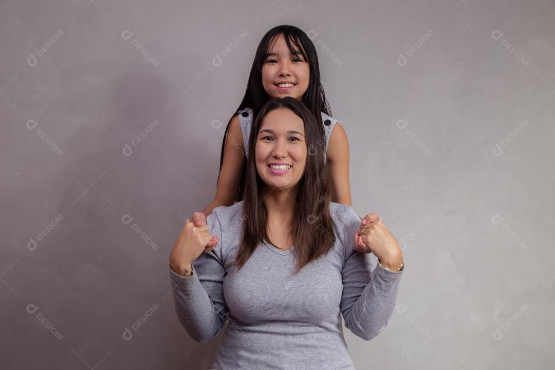 Mãe e filha abraçadas com camisetas cinzas em fundo bege