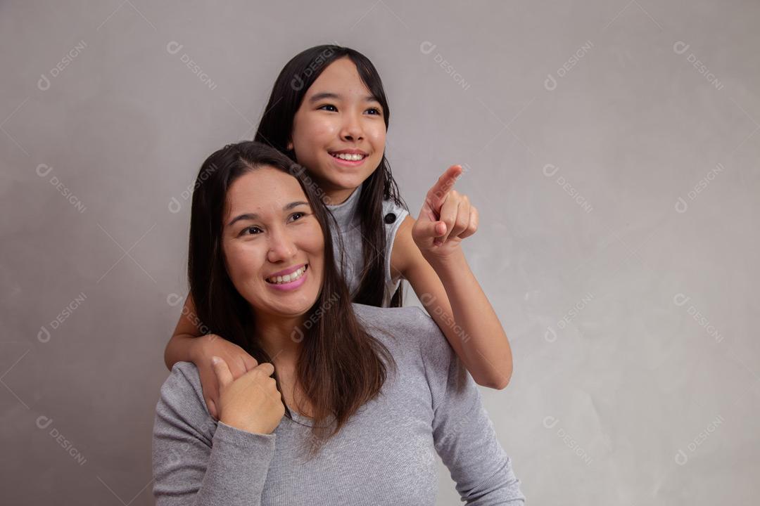 Mãe e filha abraçadas com camisetas cinzas em fundo bege