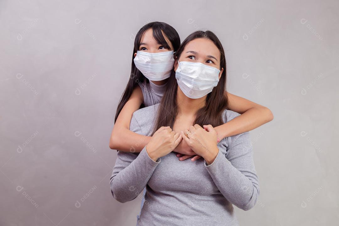 Mãe e filha abraçadas com mascaras em fundo bege