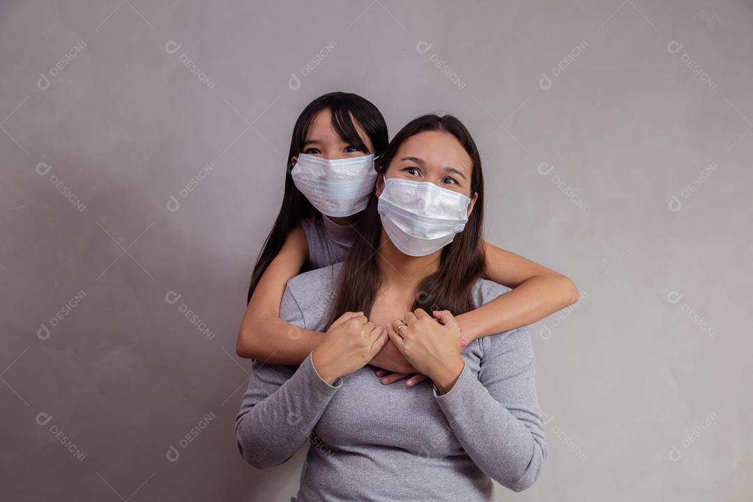 Mãe e filha abraçadas com mascaras em fundo bege