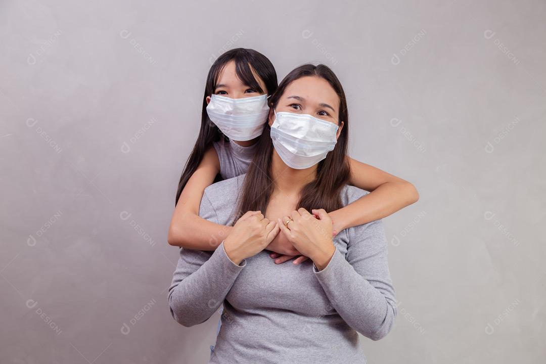Mãe e filha abraçadas com mascaras em fundo bege