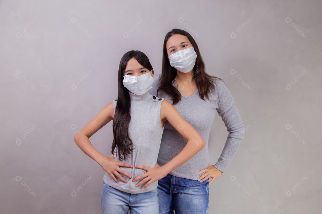 Mãe e filha abraçadas com mascaras em fundo bege