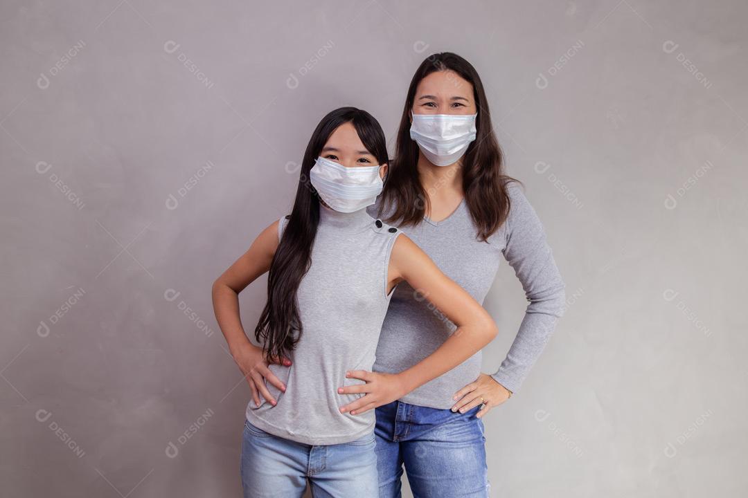 Mãe e filha abraçadas com mascaras em fundo bege