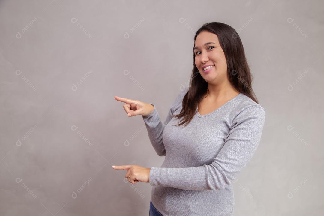 Mulher apontado para o lado e expressão de feliz em fundo cinza