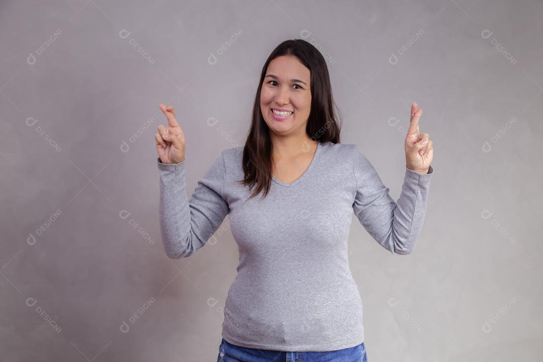 Mulher fazendo gesto de promessa e expressão de feliz em fundo cinza