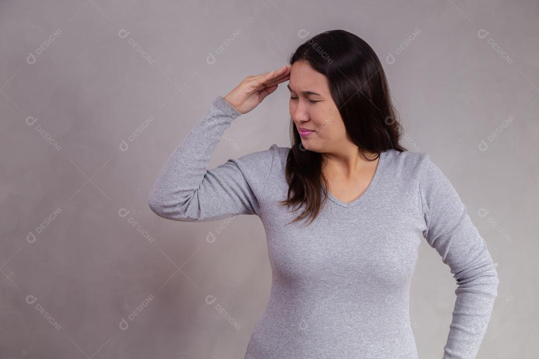 Mulher com a mão na cabeça e expressão de triste em fundo cinza