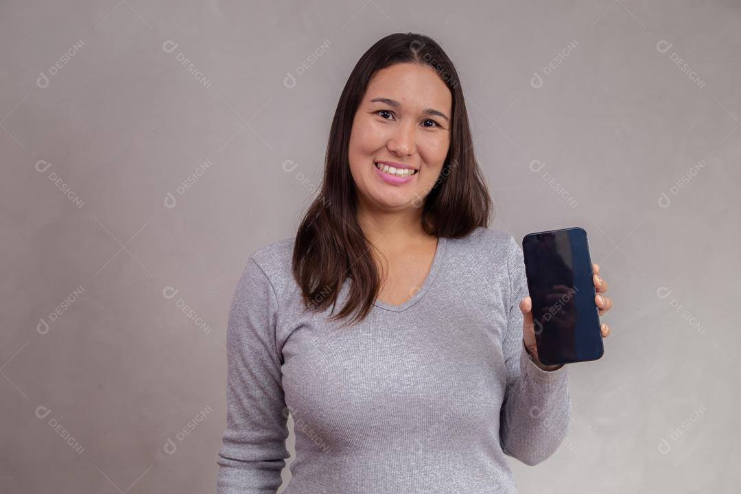 Mulher com expressão de feliz segurando celular em fundo cinza