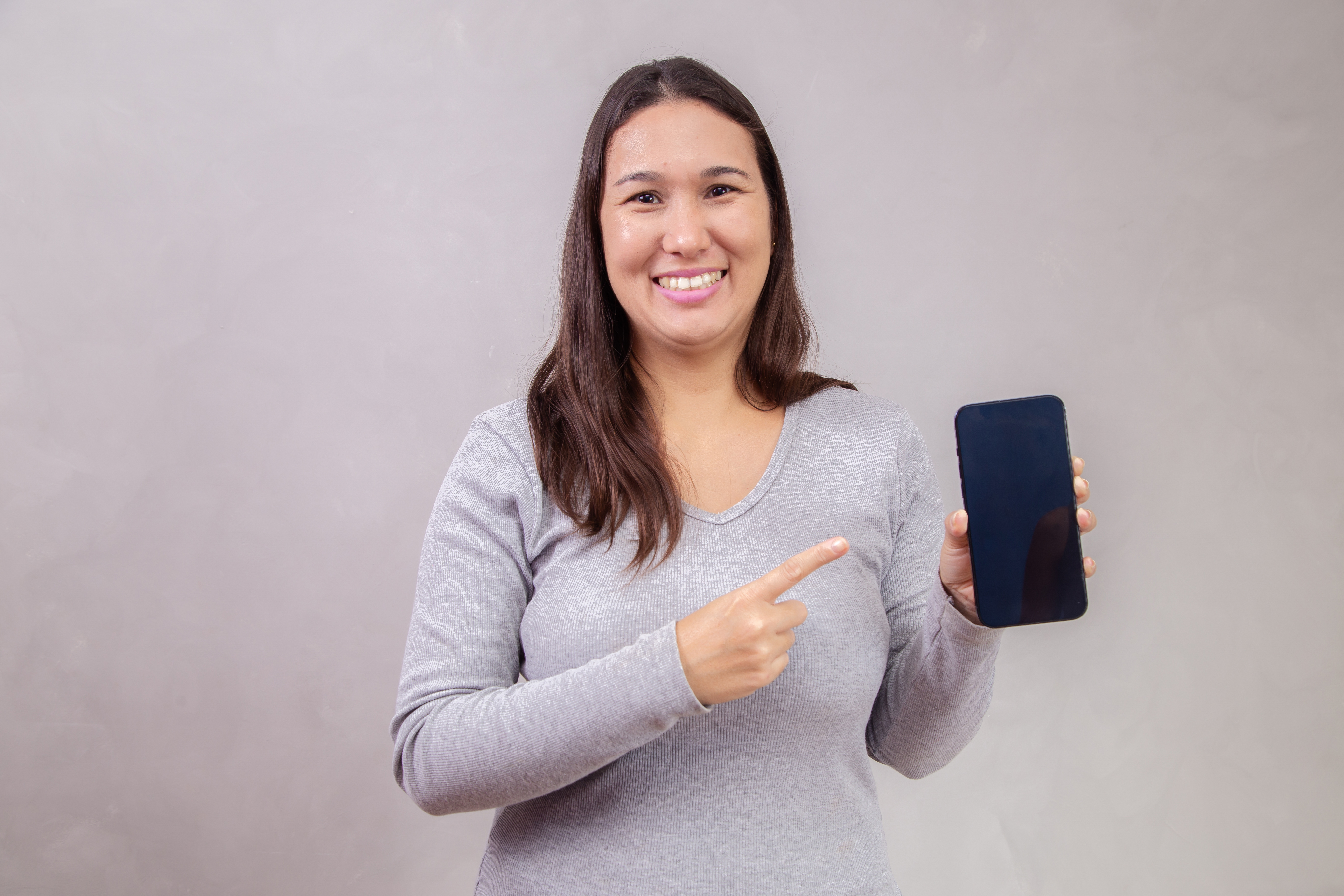 Mulher com expressão de feliz segurando celular em fundo cinza