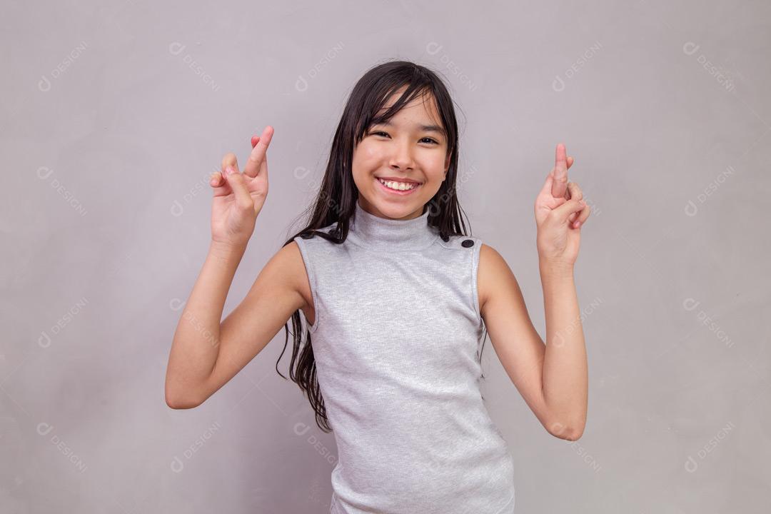 Criança japonesa de fazendo gesto de Promessa com expressão de feliz em fundo cinza