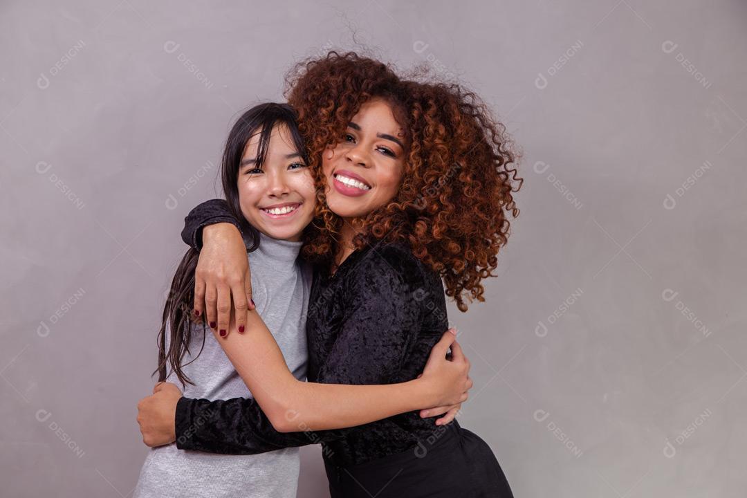 Mãe e filha abraçadas com expressões de feliz em fundo cinza