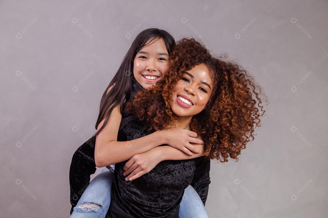 Mãe e filha abraçadas com expressões de feliz em fundo cinza