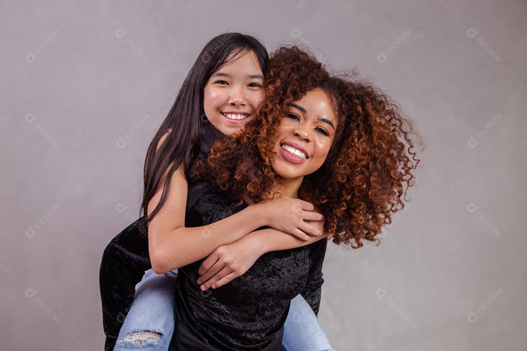 Mãe e filha abraçadas com expressões de feliz em fundo cinza