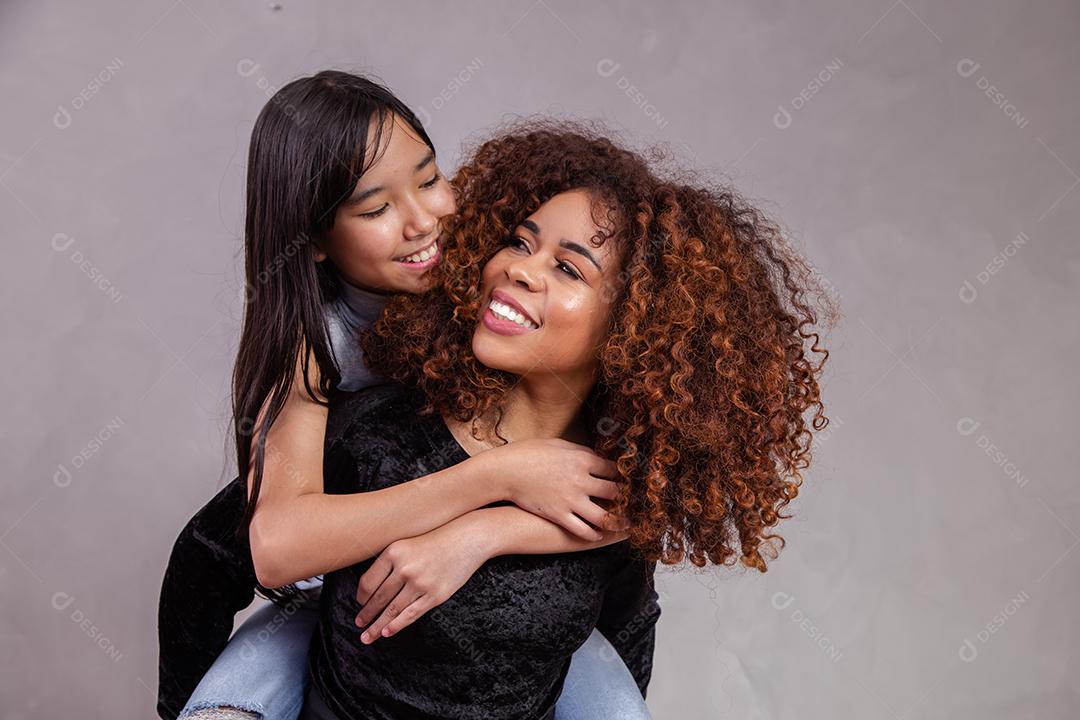 Mãe e filha abraçadas com expressões de feliz em fundo cinza