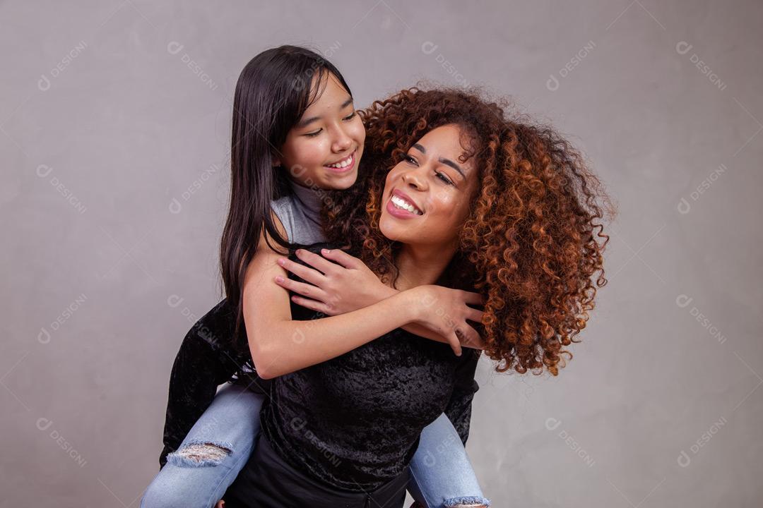 Mãe e filha abraçadas com expressões de feliz em fundo cinza