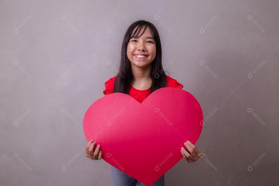 Criança japonesa segurando um cartão em forma de coração em fundo cinza
