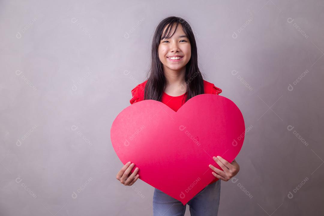 Criança japonesa segurando um cartão em forma de coração em fundo cinza