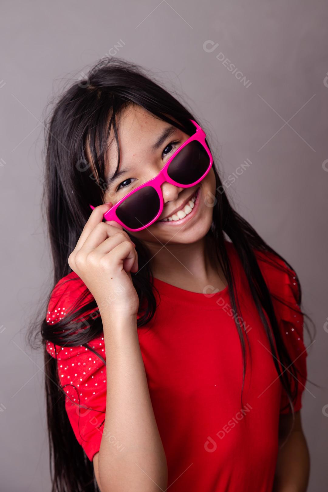 Criança japonesa com com óculos escuro rosa e roupa vermelha em fundo cinza