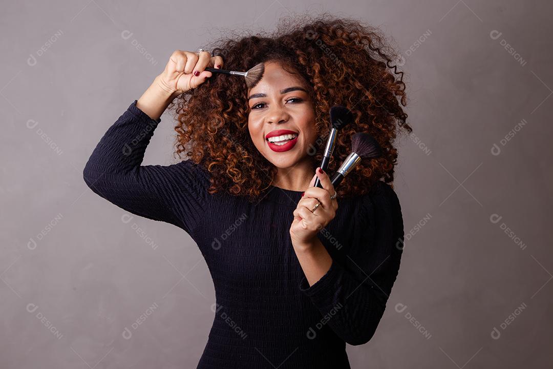 Maquiadora profissional afro segurando pincéis de maquiagem