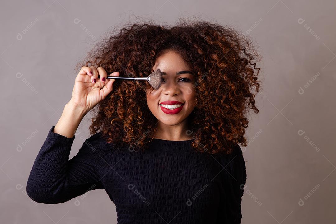 Maquiadora profissional afro segurando pincéis de maquiagem