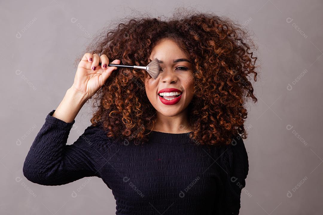 Maquiadora profissional afro segurando pincéis de maquiagem