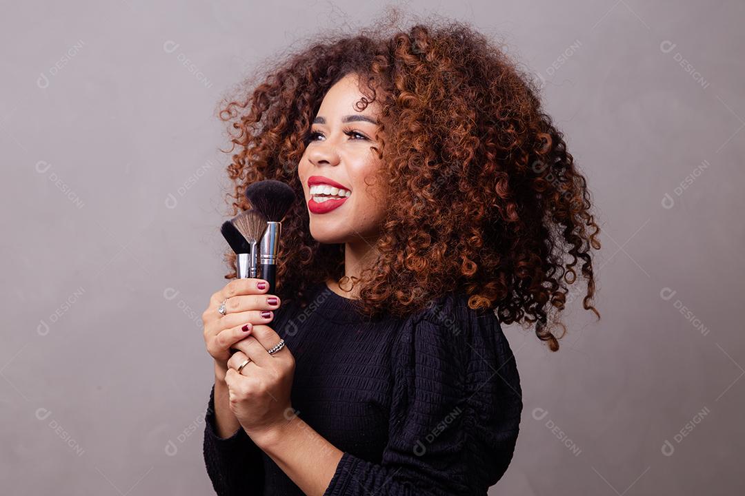Maquiadora profissional afro segurando pincéis de maquiagem