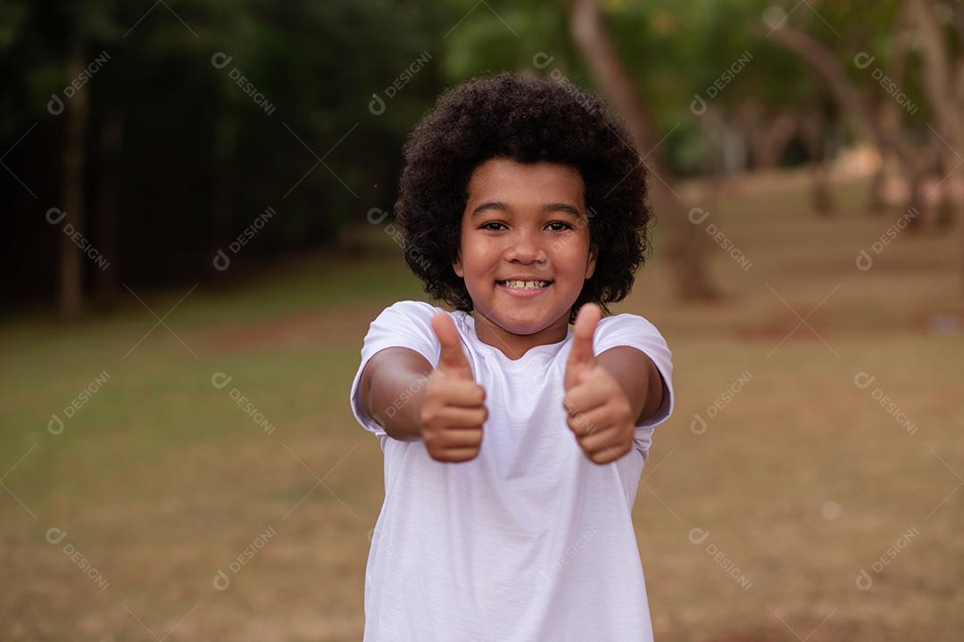 Menino afro com o polegar para cima fazendo sinal de beleza