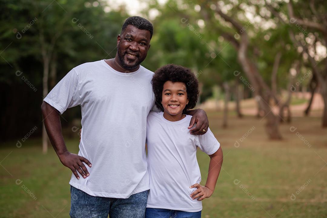 Pai e filho negros no parque abraçados sorrindo olhando para a câmera