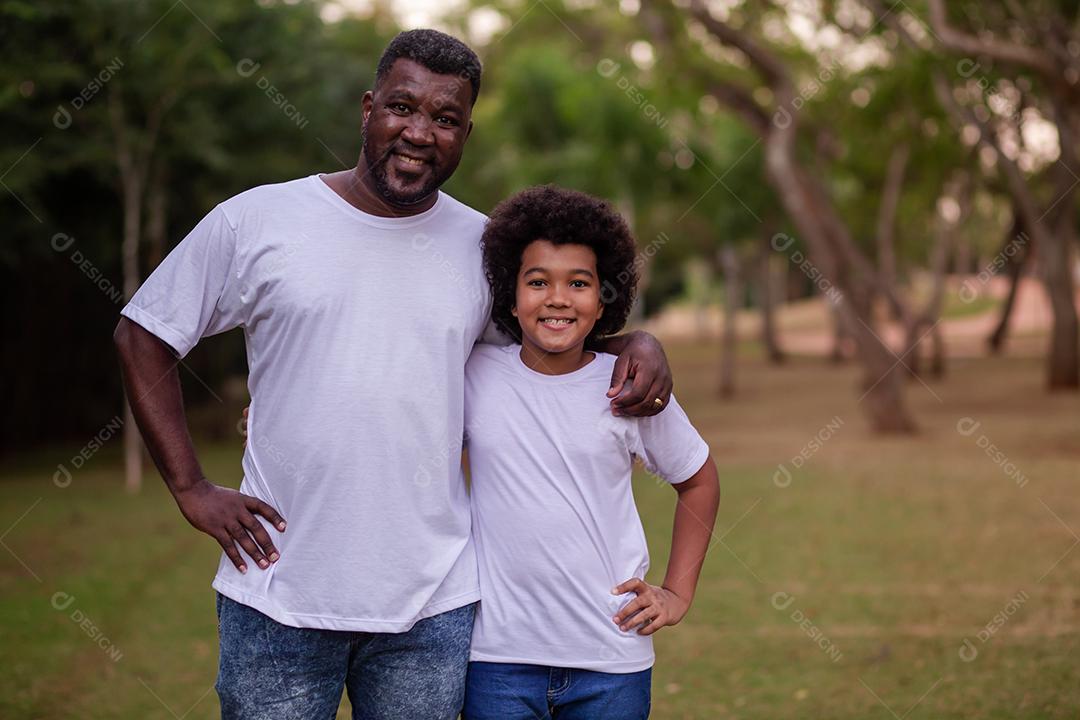 Pai e filho negros no parque abraçados sorrindo olhando para a câmera