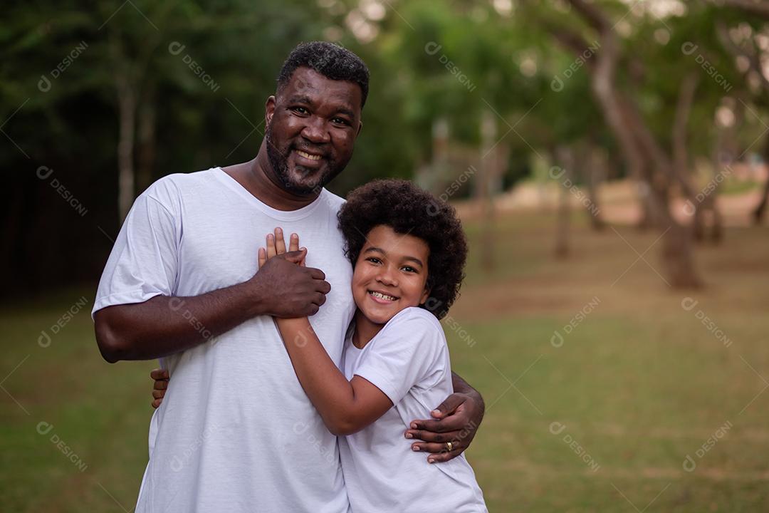 Pai e filho negros no parque abraçados sorrindo olhando para a câmera