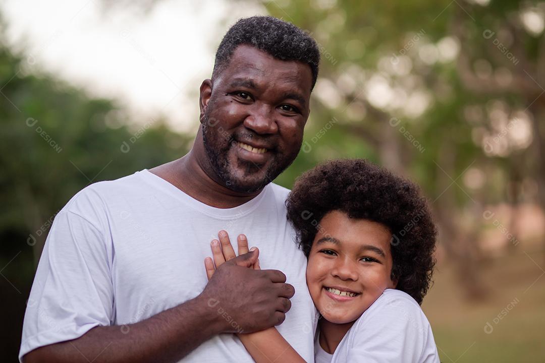 Pai e filho negros no parque abraçados sorrindo olhando para a câmera