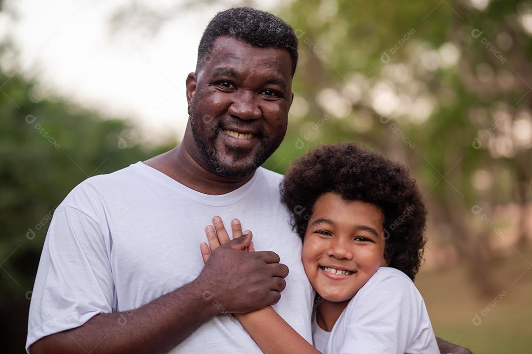 Pai e filho negros no parque abraçados sorrindo olhando para a câmera