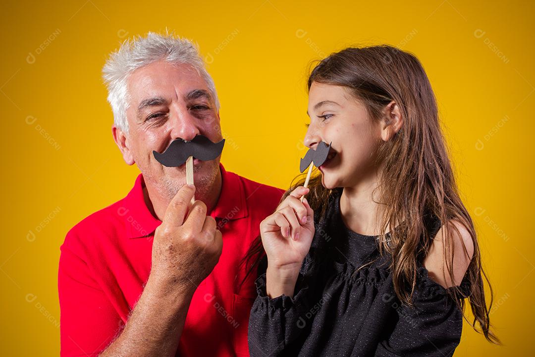 Dia dos Pais. Filha feliz segurando um bigode de papel com o pai em fundo amarelo. filha e pai com bigode de férias