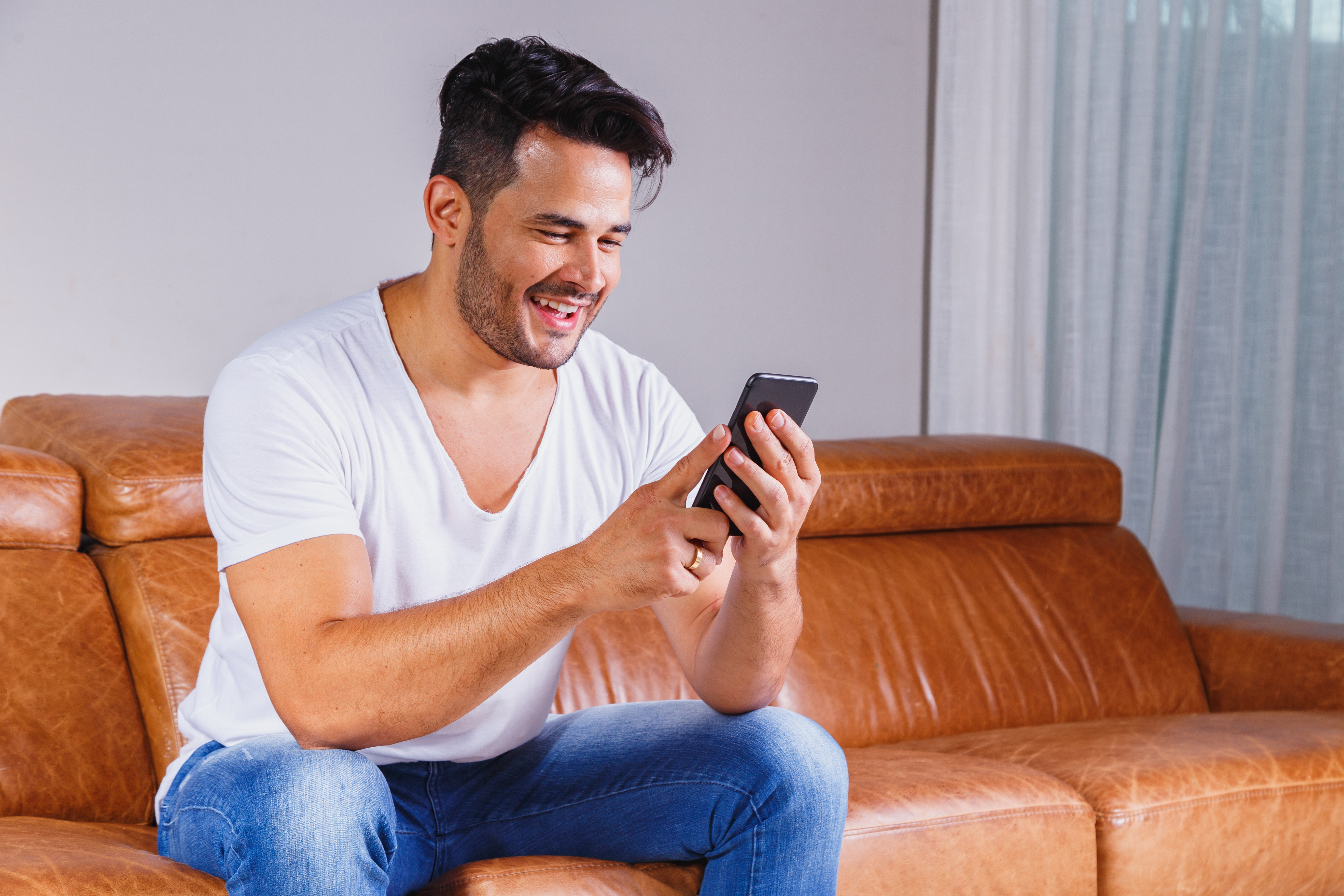 Homem sentado no sofá de casa segurando celular