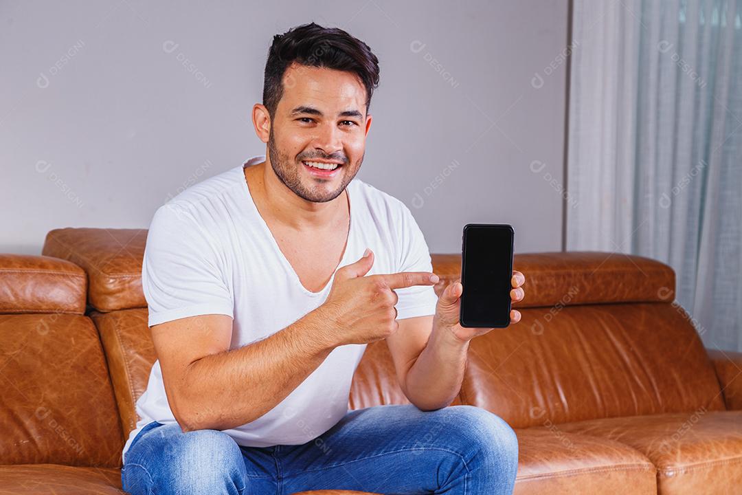 Homem sentado no sofá de casa segurando celular