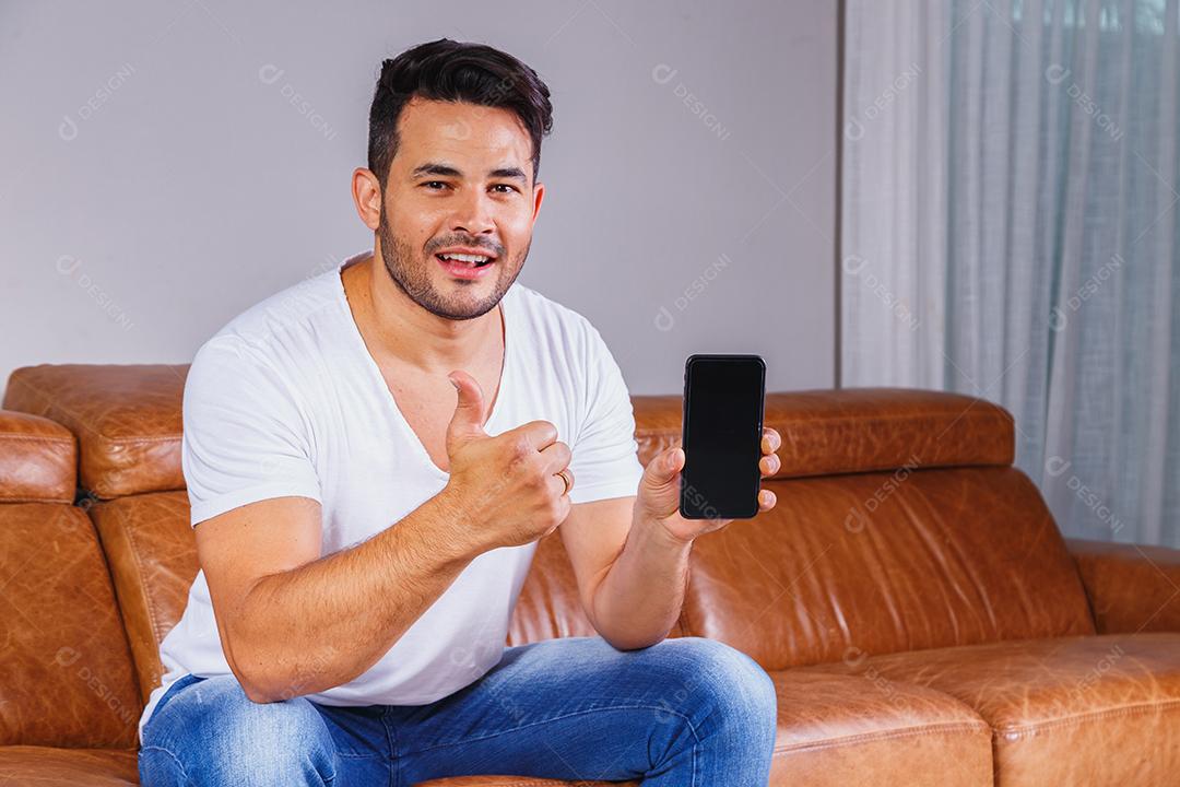 Homem sentado no sofá de casa segurando celular