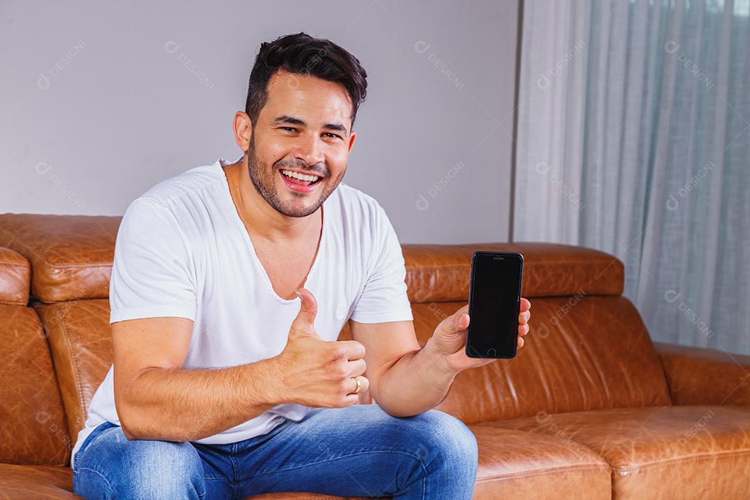 Homem sentado no sofá de casa segurando celular