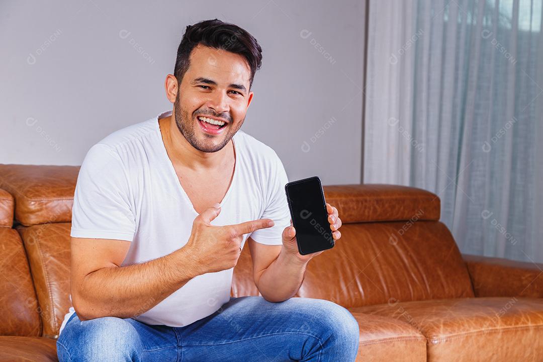 Homem sentado no sofá de casa segurando celular