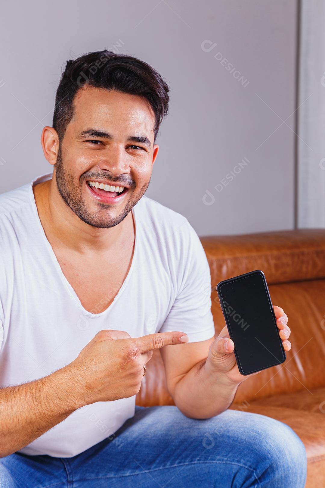 Homem sentado no sofá de casa segurando celular