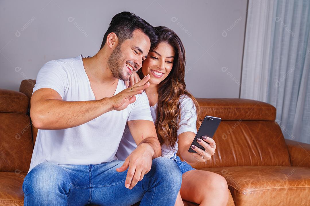 Homem e mulher sentado no sofá de casa segurando celular