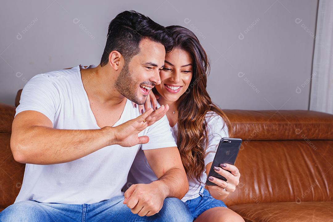 Homem e mulher sentado no sofá de casa segurando celular