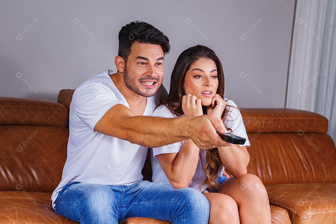 Homem e mulher sentado no sofá de casa assistindo tv