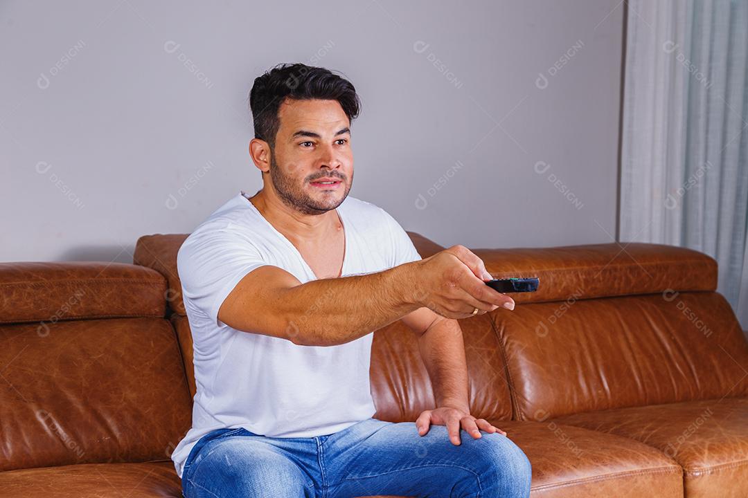 Homem sentado no sofá de casa assistindo tv