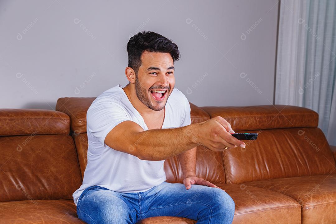 Homem sentado no sofá de casa assistindo tv