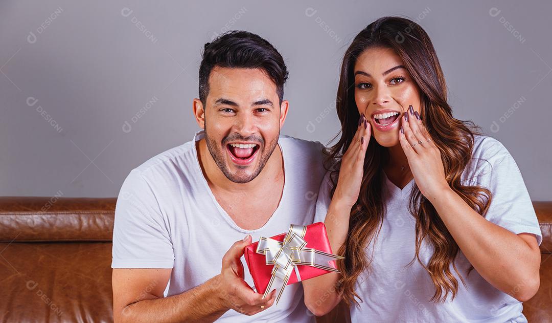 Homem sorridente surpreende a namorada com presente em casa.