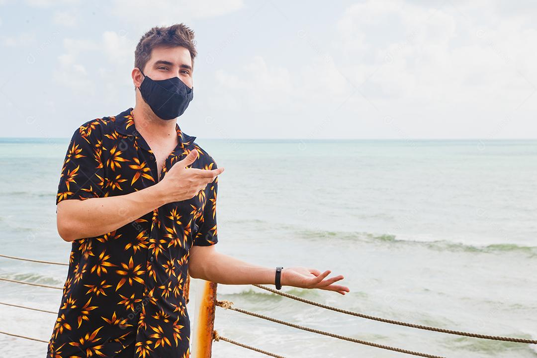 Homem em cima de ponte de biquini verde ao lado de mar segurando mascara