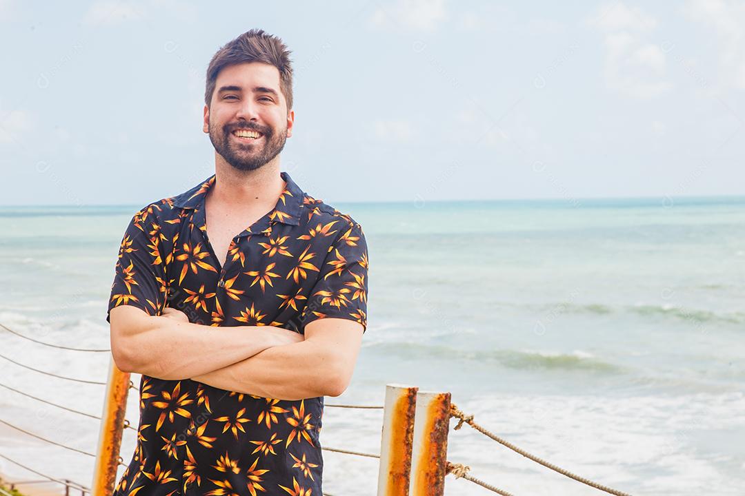 Homem em cima de ponte de biquini verde ao lado de mar segurando mascara