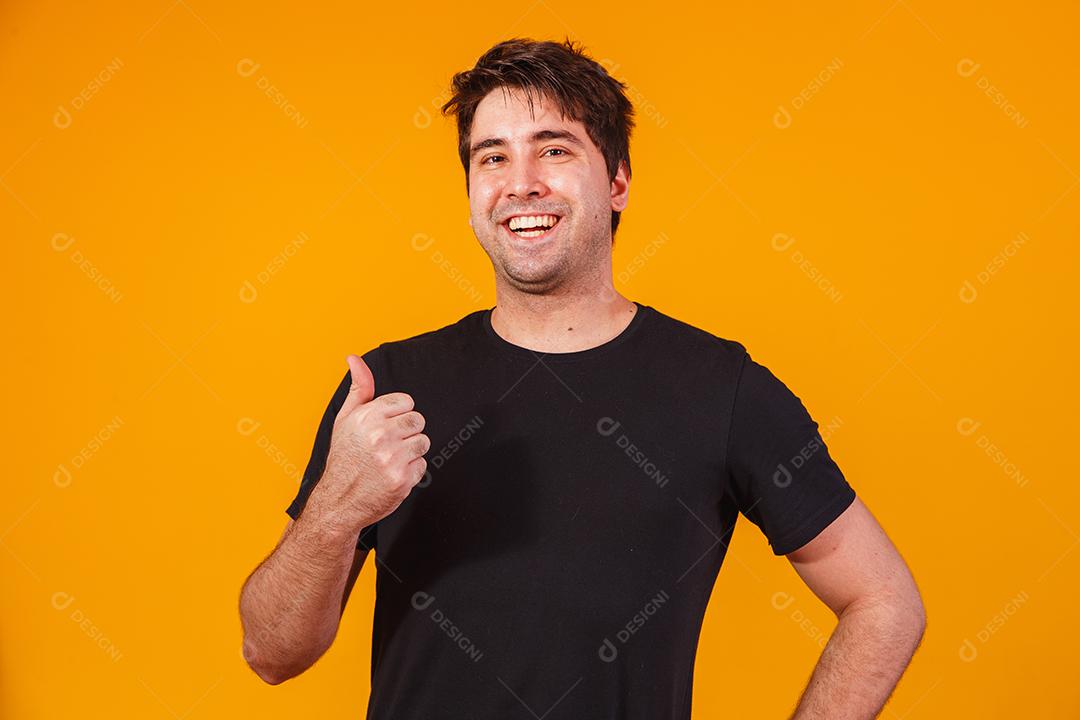 Foto de homem bonito em t-shirt casual, sorrindo para a câmera com o polegar para cima.